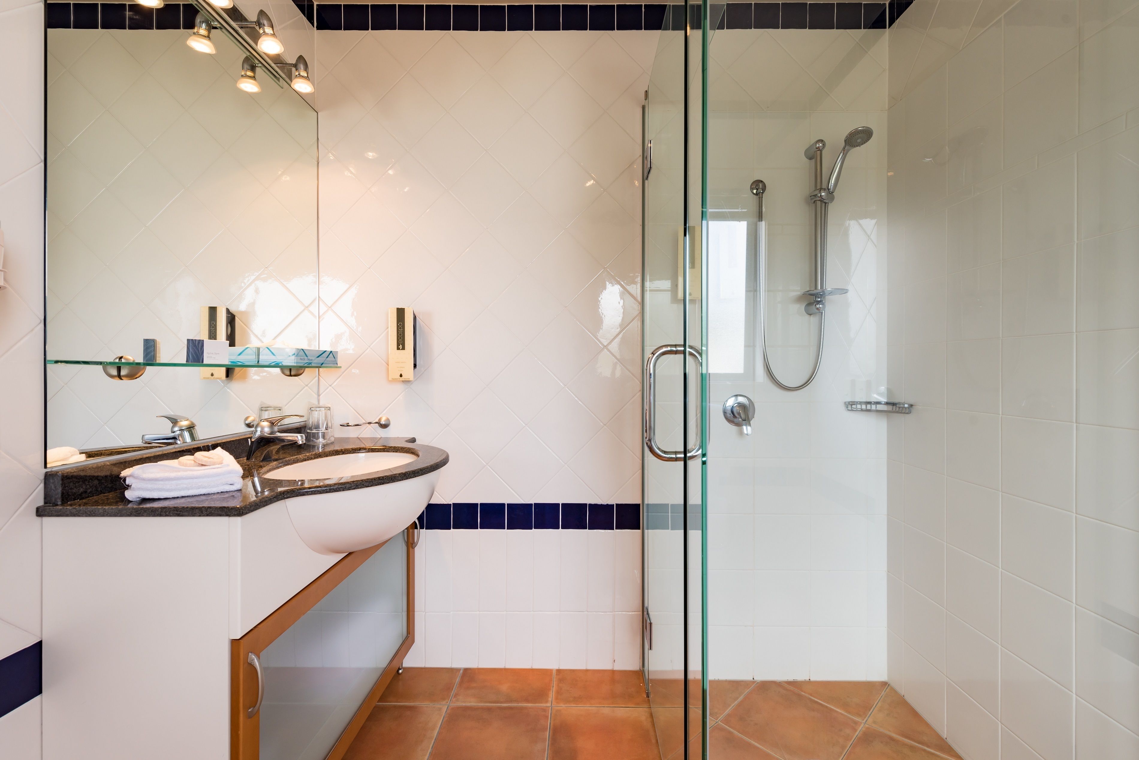A modern bathroom with a glass-enclosed shower, a white sink, and a large mirror.