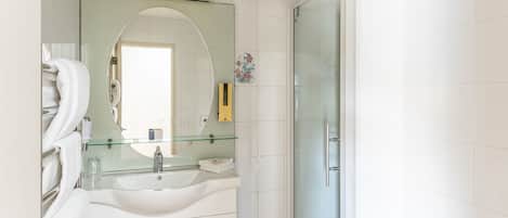Une salle de bain moderne avec une douche à parois de verre, un lavabo blanc surmonté d’un plateau en verre et un miroir au-dessus du lavabo.