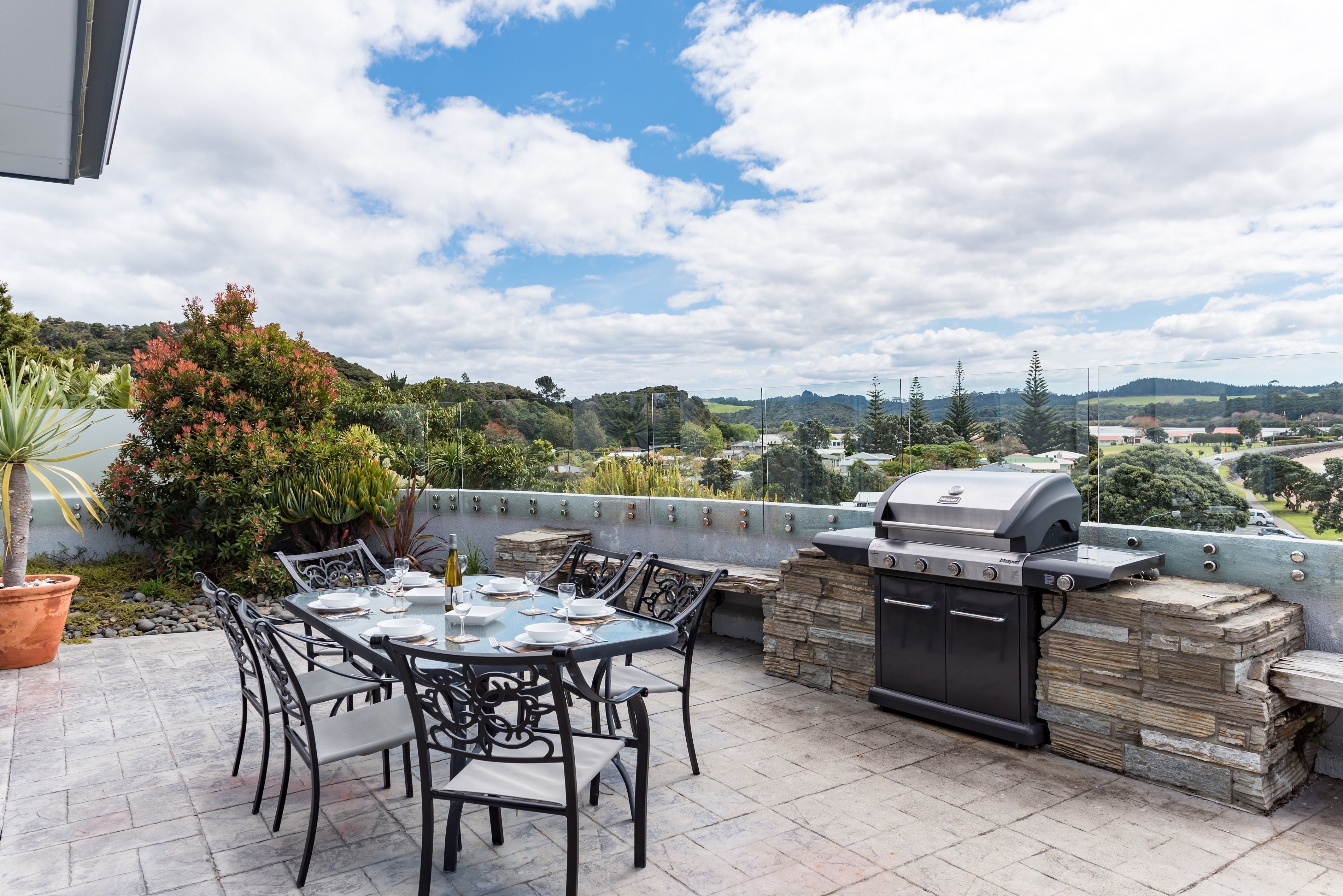 An outdoor patio with a dining table and chairs, a barbecue grill, and a stone wall.