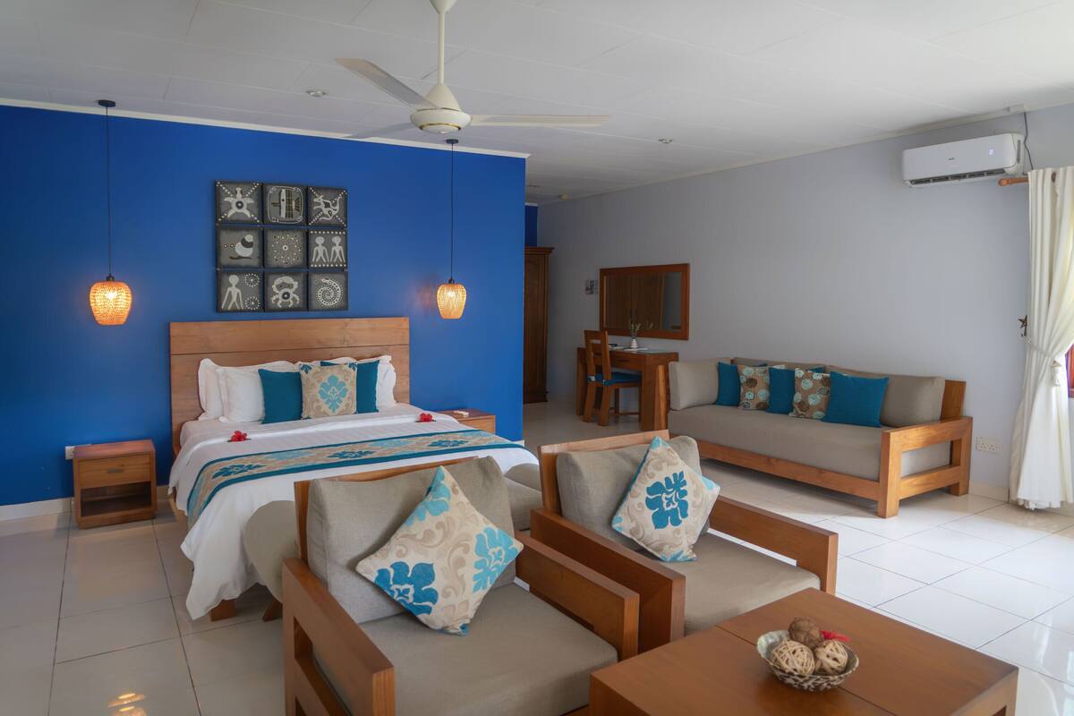A hotel room with a bed, a sofa, a dining table, and a ceiling fan.