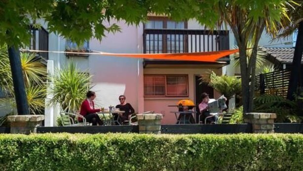 An outdoor seating area with tables and chairs, surrounded by a low hedge and palm trees. - Victoria Lodge (Rotorua)