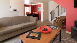 A living room with a beige sofa, a wooden coffee table with a red bowl, and a staircase with a red wall. - Victoria Lodge (Rotorua)