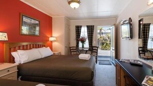 A hotel room with a bed, a desk, and a chair. There is a window with curtains and a door leading outside. - Victoria Lodge (Rotorua)