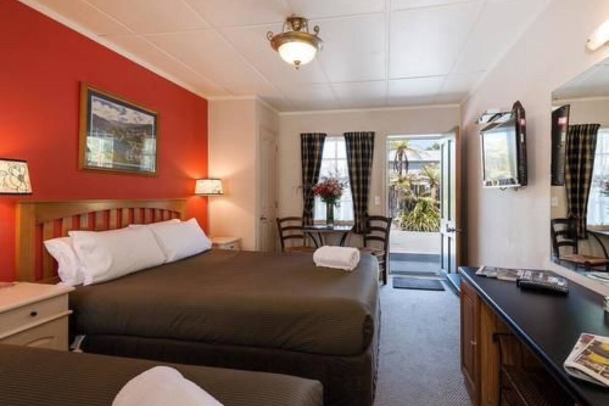 A hotel room with a bed, a desk, and a chair. There is a window with curtains and a door leading outside.