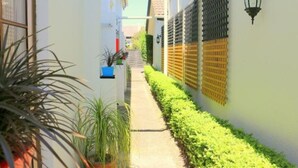 A narrow alleyway with a concrete path flanked by white walls and green plants. - Victoria Lodge (Rotorua)