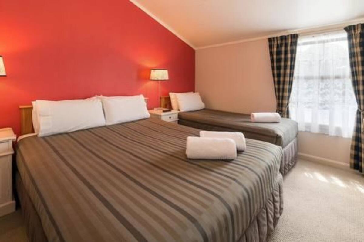 A hotel room with two beds, each with striped bedding and white pillows. There are two bedside tables with lamps, and the room has a red accent wall.