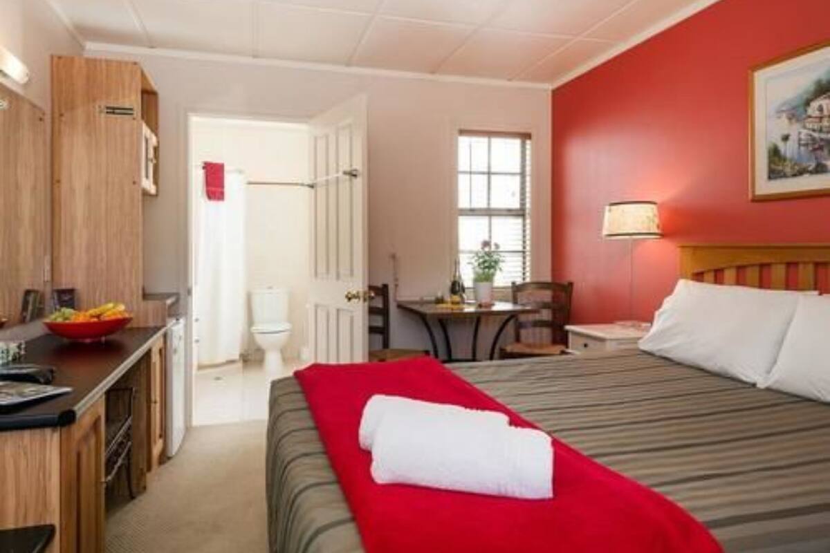 A hotel room with a bed, a desk, a chair, a window, and a door.