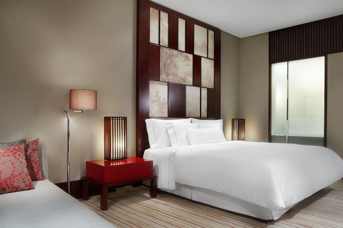 A hotel room with a large bed, a nightstand with a lamp, and a wall with artwork.