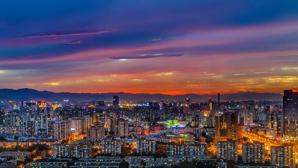 A cityscape at dusk with illuminated buildings and a mountain range in the background. - The Westin Beijing Chaoyang (Beijing)