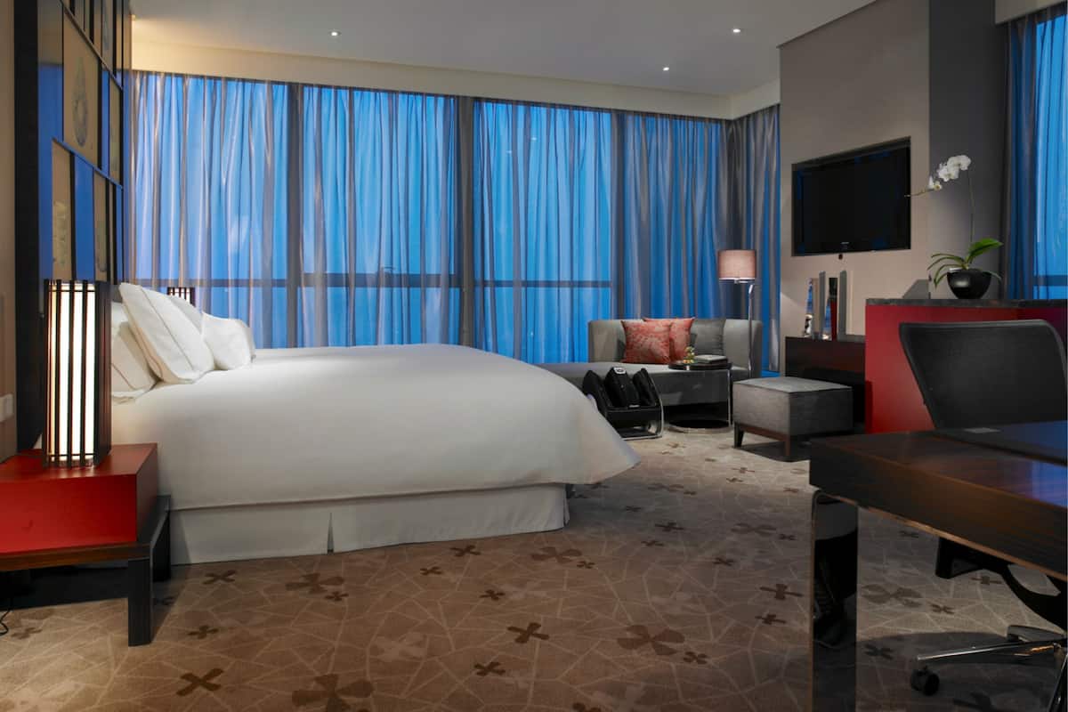 A hotel room with a large bed, a desk, a chair, a TV, and a window with curtains.