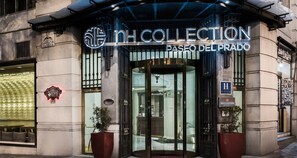 La entrada del NH Collection Paseo del Prado con una puerta de cristal y un cartel encima.