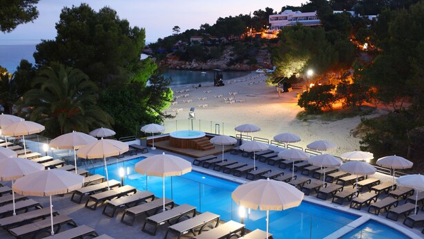 A pool area with sun loungers and umbrellas, a beach in the background, and a view of the sea. - Sandos El Greco Hotel - Adults Only (Sant Joan de Labritja)