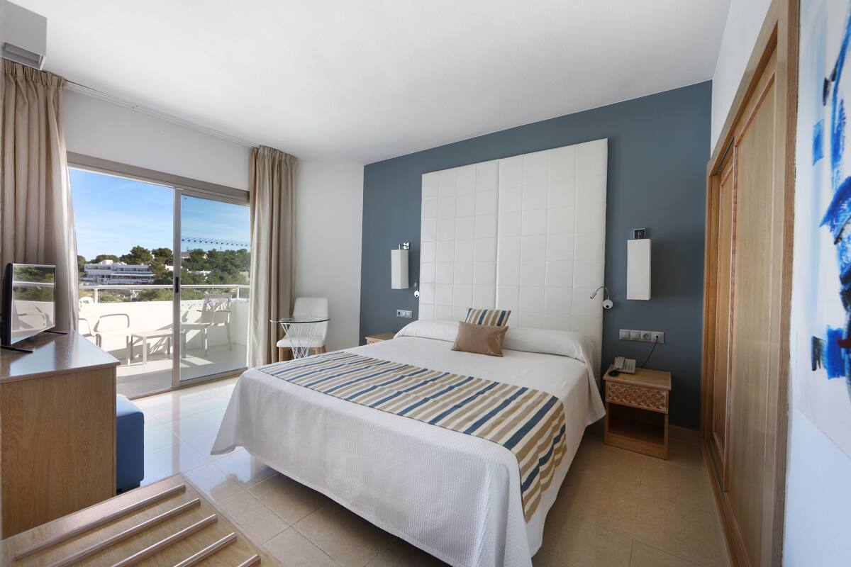 Une chambre d’hôtel avec un grand lit, un bureau, une chaise, une petite table et une vue sur l’extérieur.