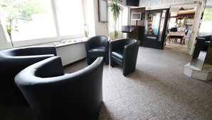 A hotel lobby with black leather chairs, a large window, a radiator, a plant, and a door leading to a dining area. - Hotel Europa Offenbach (Offenbach am Main)
