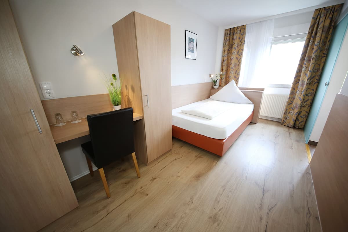 Een compacte hotelkamer met een houten bureau, een bed en een raam met gordijnen.