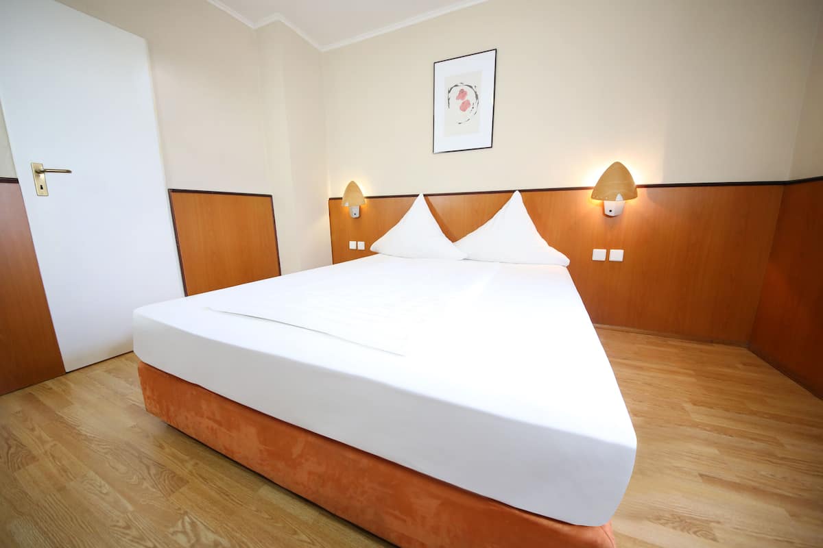 Een hotelkamer met een groot bed, een houten hoofdbord, twee wandlampen en een ingelijst schilderij aan de muur.