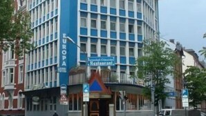 A corner building with a blue and white facade, a sign for 'Europa Hotel', and a restaurant sign below. - Hotel Europa Offenbach (Offenbach am Main)