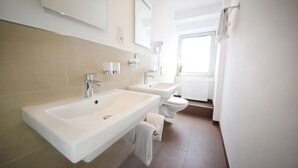 A modern bathroom with two sinks, a toilet, and a large mirror. - Hotel Europa Offenbach (Offenbach am Main)