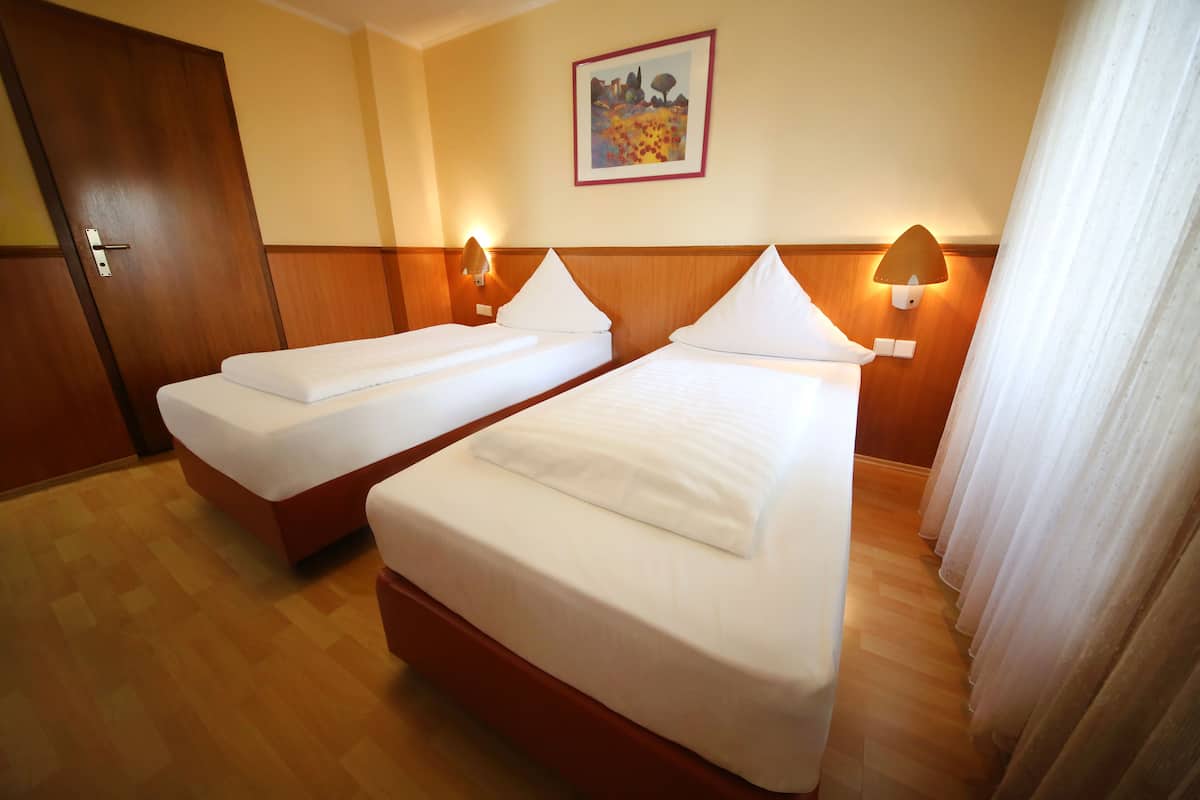 Een hotelkamer met twee bedden, houten vloeren, een schilderij aan de muur en een deur.