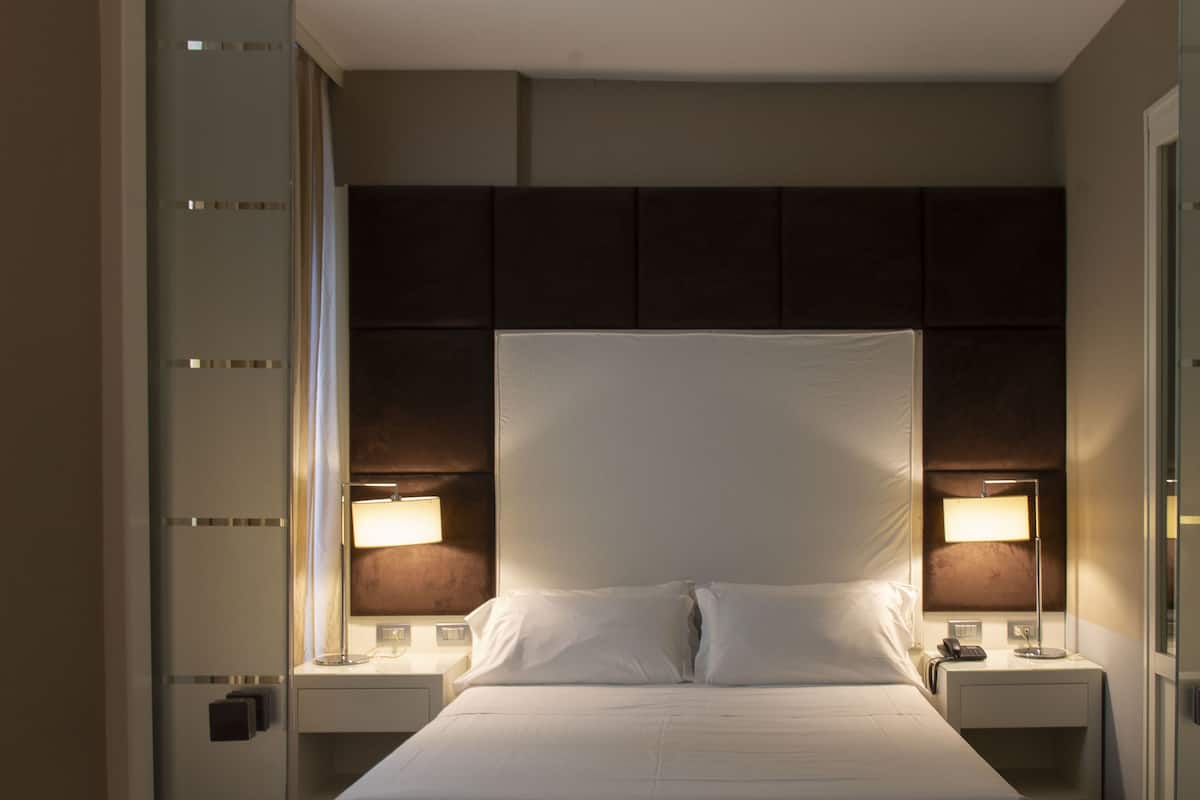 Ein Hotelzimmer mit einem großen Bett, zwei Nachttischen mit Lampen und einem Kopfteil mit integriertem Regal.