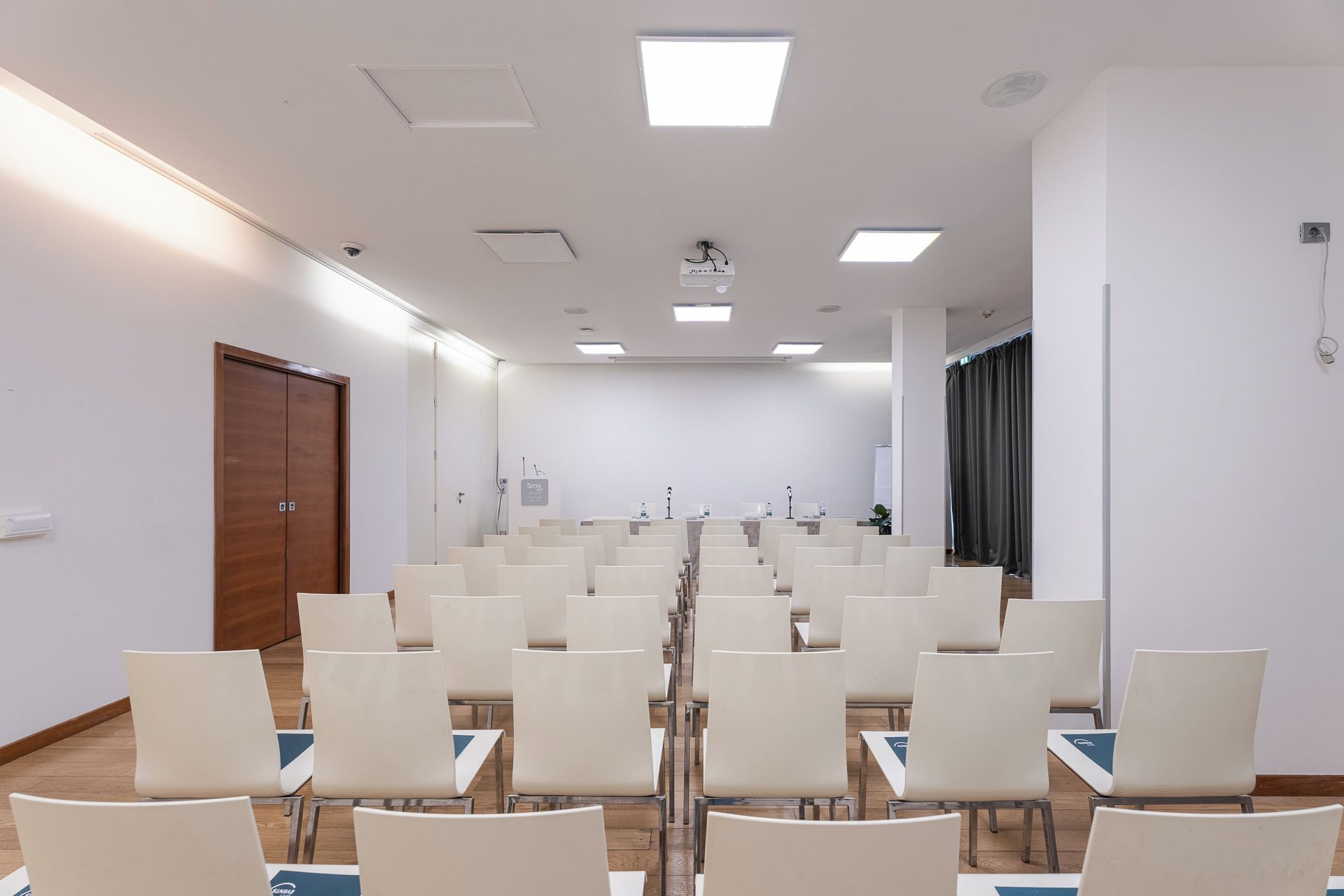 Een vergaderzaal met rijen stoelen, een spreekgestoelte en een deur.