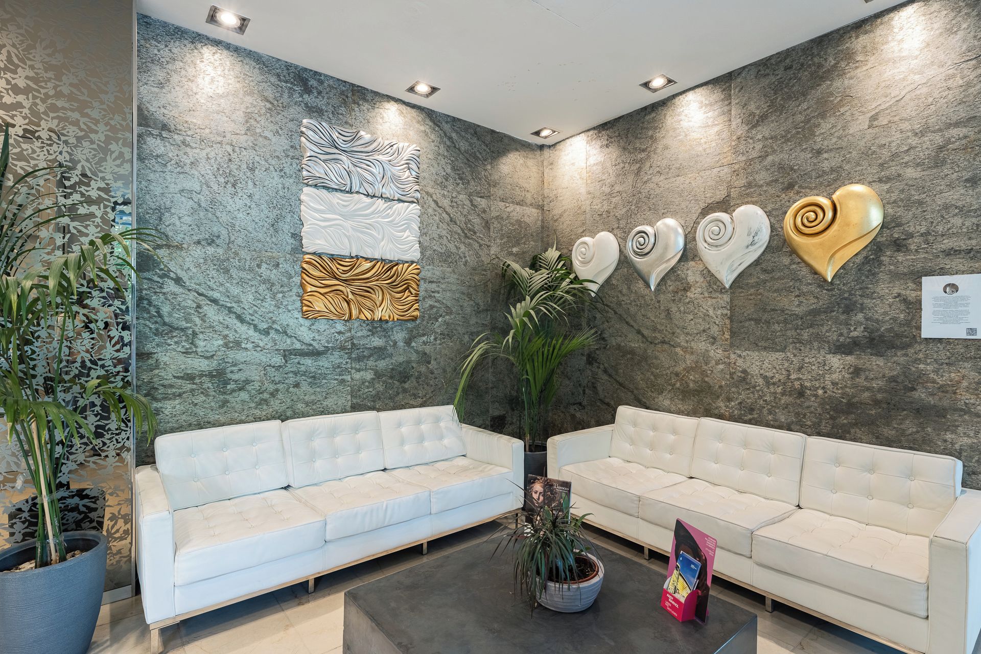 Un'area reception con due divani bianchi, un'ampia parete decorativa e una pianta in vaso.