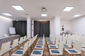 Une salle de conférence avec des rangées de chaises, un projecteur et un tableau blanc.