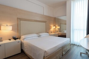 Ein Hotelzimmer mit einem großen Bett, Nachttischen, einem Schreibtisch und einem Spiegel.