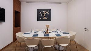 A conference room with a round table, six chairs, water bottles, a vase with dried flowers, and a black and gold abstract painting on the wall. - Smy Bologna Centrale (Bologna)