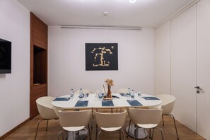 Ein Konferenzraum mit einem runden Tisch, sechs Stühlen, Wasserflaschen, einer Vase mit getrockneten Blumen und einem schwarz-goldenen abstrakten Gemälde an der Wand.