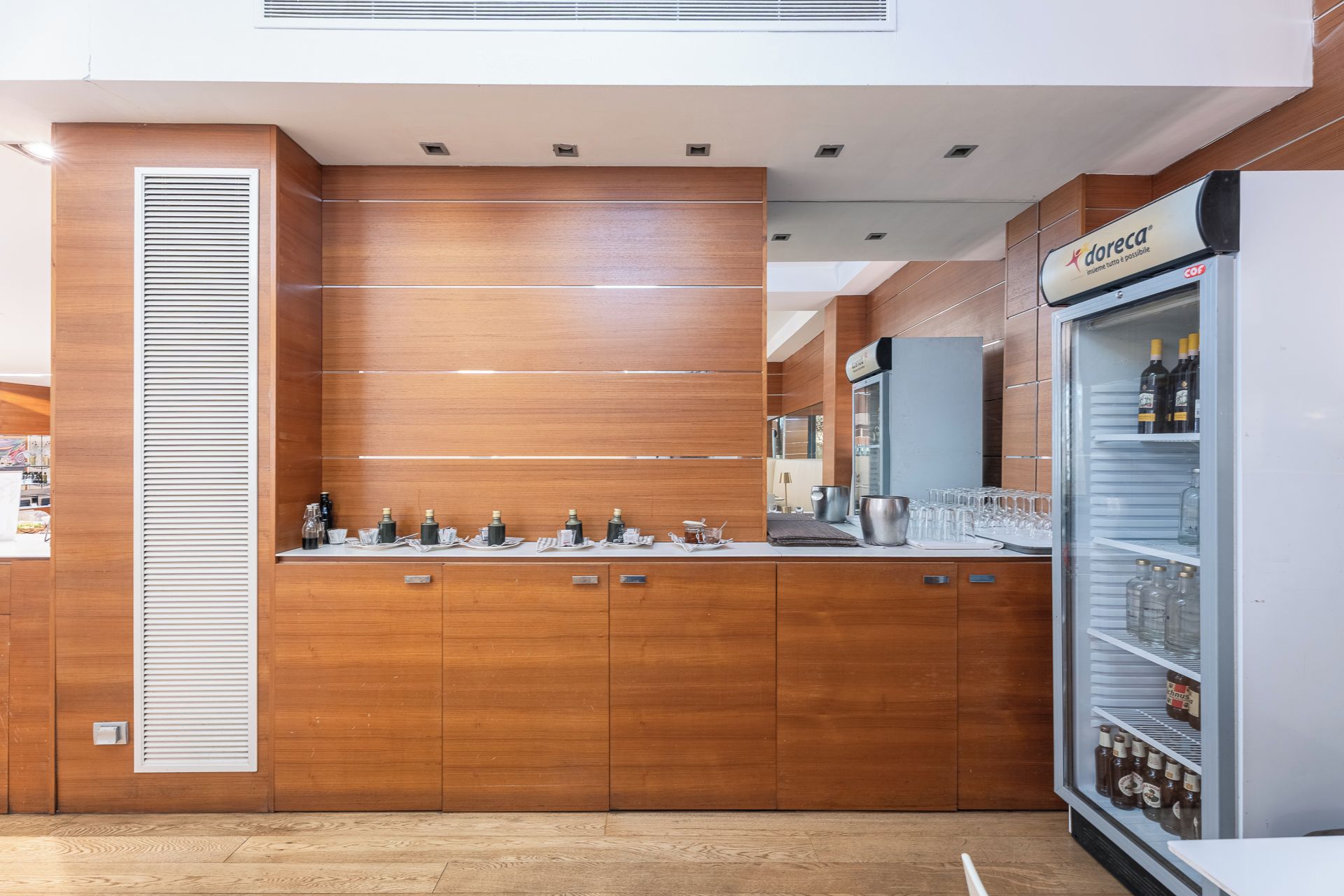 Un área de bar moderna con mostrador de madera, un miniibar y un refrigerador lleno de bebidas.
