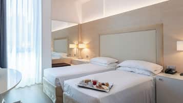 A hotel room with two beds, a desk, a chair, and a breakfast tray on the bed.