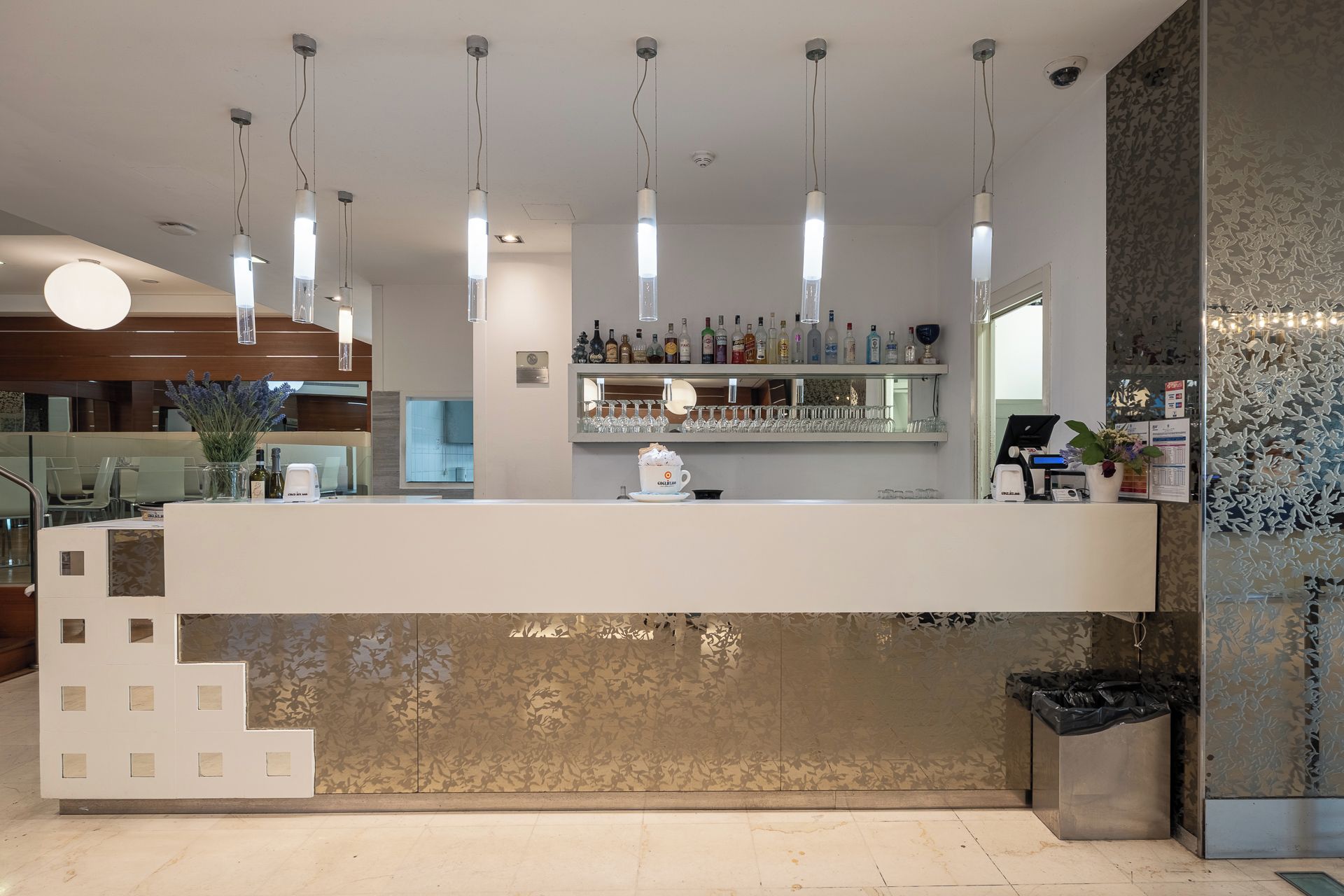 Een moderne bar met een toog, hangende verlichting en een decoratieve wand.