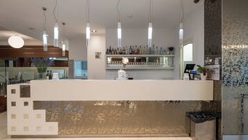 Een moderne bar met een toog, hangende verlichting en een decoratieve wand.