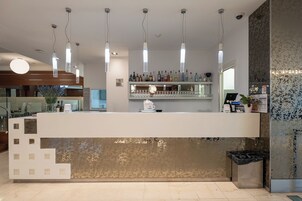 Een moderne bar met een toog, hangende verlichting en een decoratieve wand.