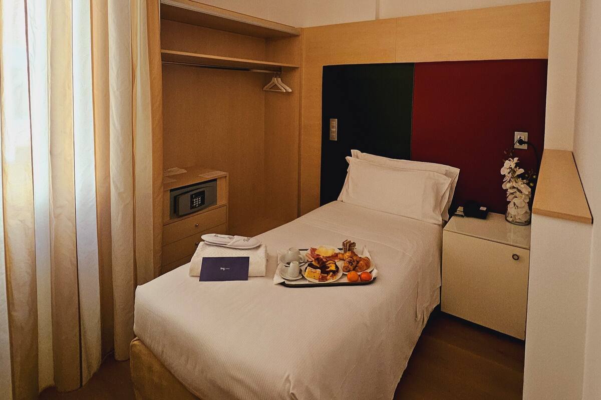 A hotel room with a bed, bedside table, and a small desk with a lamp.