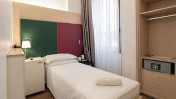 Een hotelkamer met een bed, een bureau met lamp, een telefoon, een nachtkastje met koffiezetapparaat en een kledingkast.