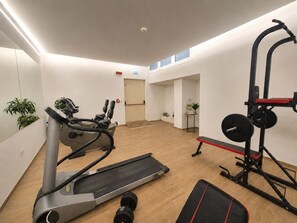Ein Fitnessraum mit Cardiogeräten, Kurzhanteln und einem Spiegel.