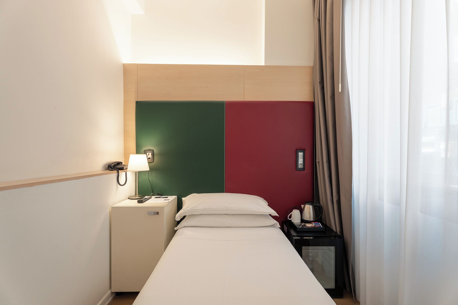 Habitación de hotel con cama, mesita de noche, lámpara y teléfono.