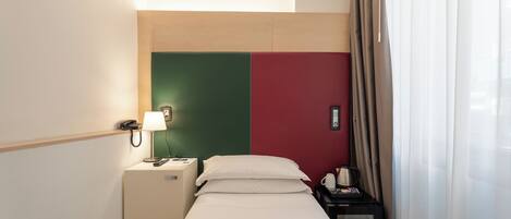Habitación de hotel con cama, mesita de noche, lámpara y teléfono.
