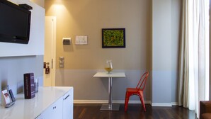 A hotel room with a flat-screen TV, a small table with a glass vase, a red chair, and a painting on the wall. - Smy Bologna Centrale (Bologna)