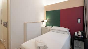 Una camera d'albergo con un letto, un comodino con una lampada, un telefono e un piccolo armadietto.