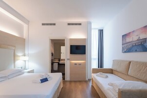 Habitación de hotel con cama, sofá, televisor y un cuadro en la pared.