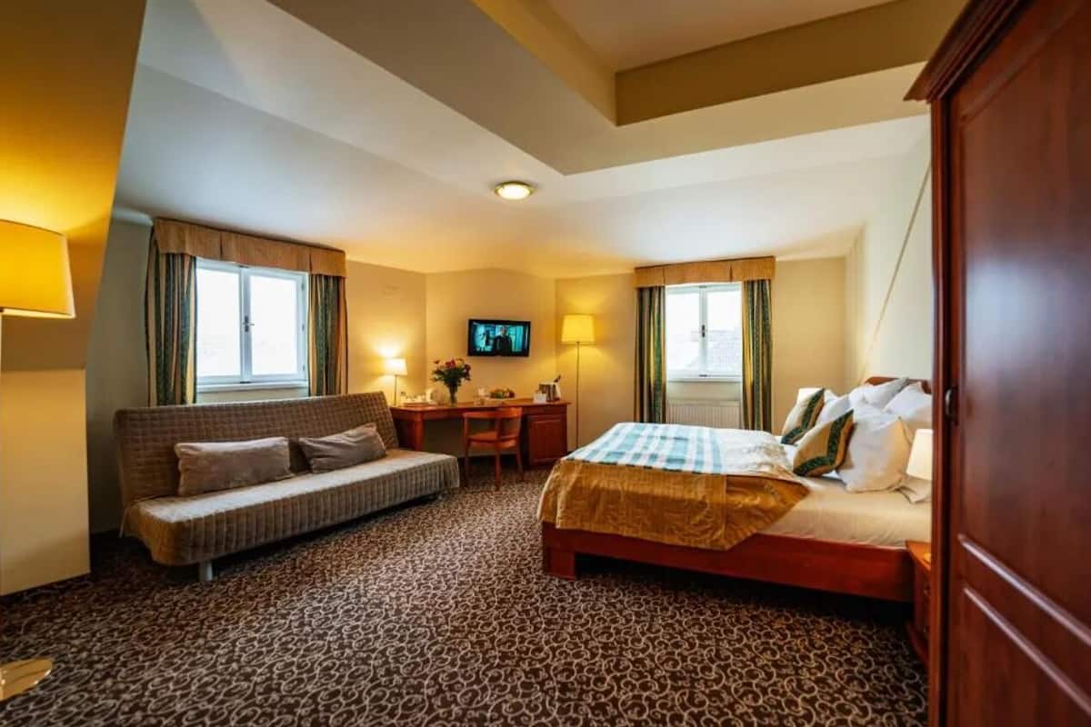 A hotel room with a bed, a sofa, a desk, and a television.