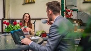 A person using a laptop at a table with a glass top, surrounded by potted plants and flowers. - Hotel U Divadla (Prague)