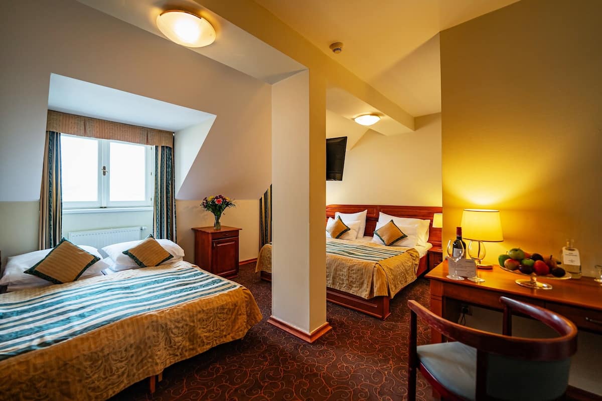 A hotel room with two beds, a desk with a lamp, and a chair.