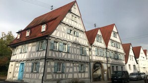 A traditional half-timbered building with a steeply pitched red-tiled roof, multiple windows with shutters, and a prominent entrance with an archway. - Historikhotel Ochsen (Tamm)