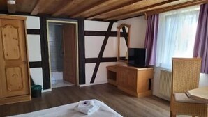 A room with a bed, a wooden desk, a chair, a television, and a window with curtains. - Historikhotel Ochsen (Tamm)