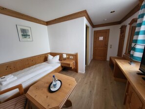 A small, cozy room with a single bed, a wooden table with a bottle, a chair, and a desk with a lamp. - Historikhotel Ochsen (Tamm)
