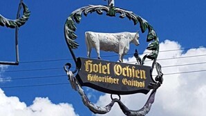 A sign for Hotel Ochsen with a cow and decorative elements. - Historikhotel Ochsen (Tamm)